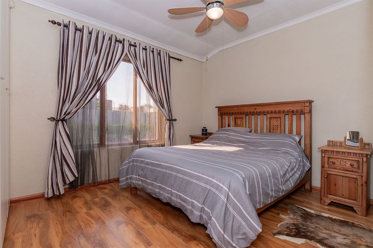A well-lit bedroom featuring wood-look laminate flooring, a ceiling fan, and a window with curtain treatments.