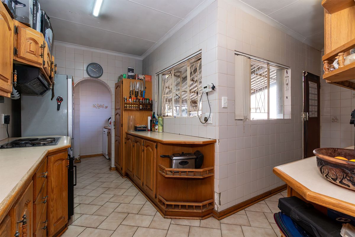 A dated kitchen featuring wooden cabinetry, tiled walls, and a functional layout with an adjacent scullery area.