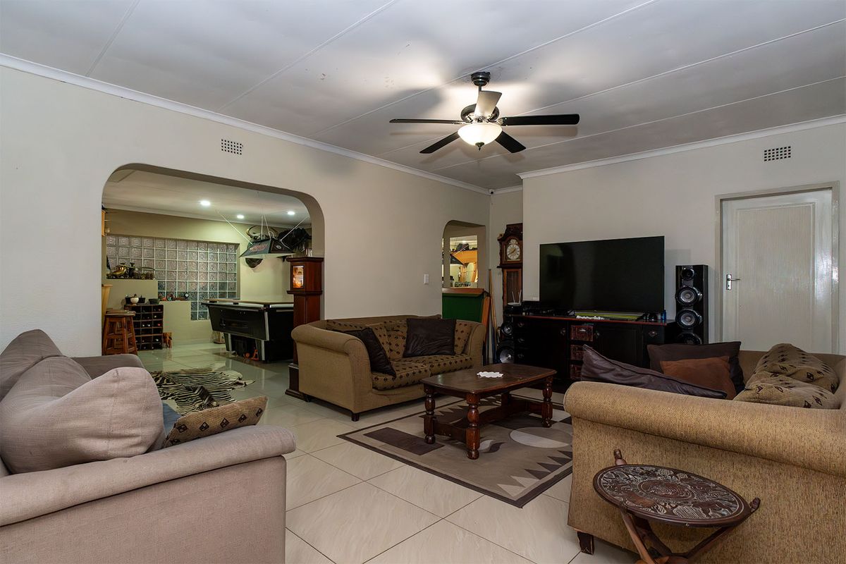 Spacious living area featuring tiled flooring, a ceiling fan, and an arched entryway leading to an adjacent entertainment space with glass block accents.