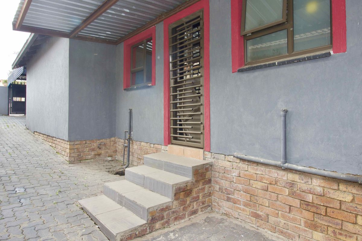 Exterior view of the property featuring a paved walkway, tiled entrance steps, security gate, and a covered lean-to structure.