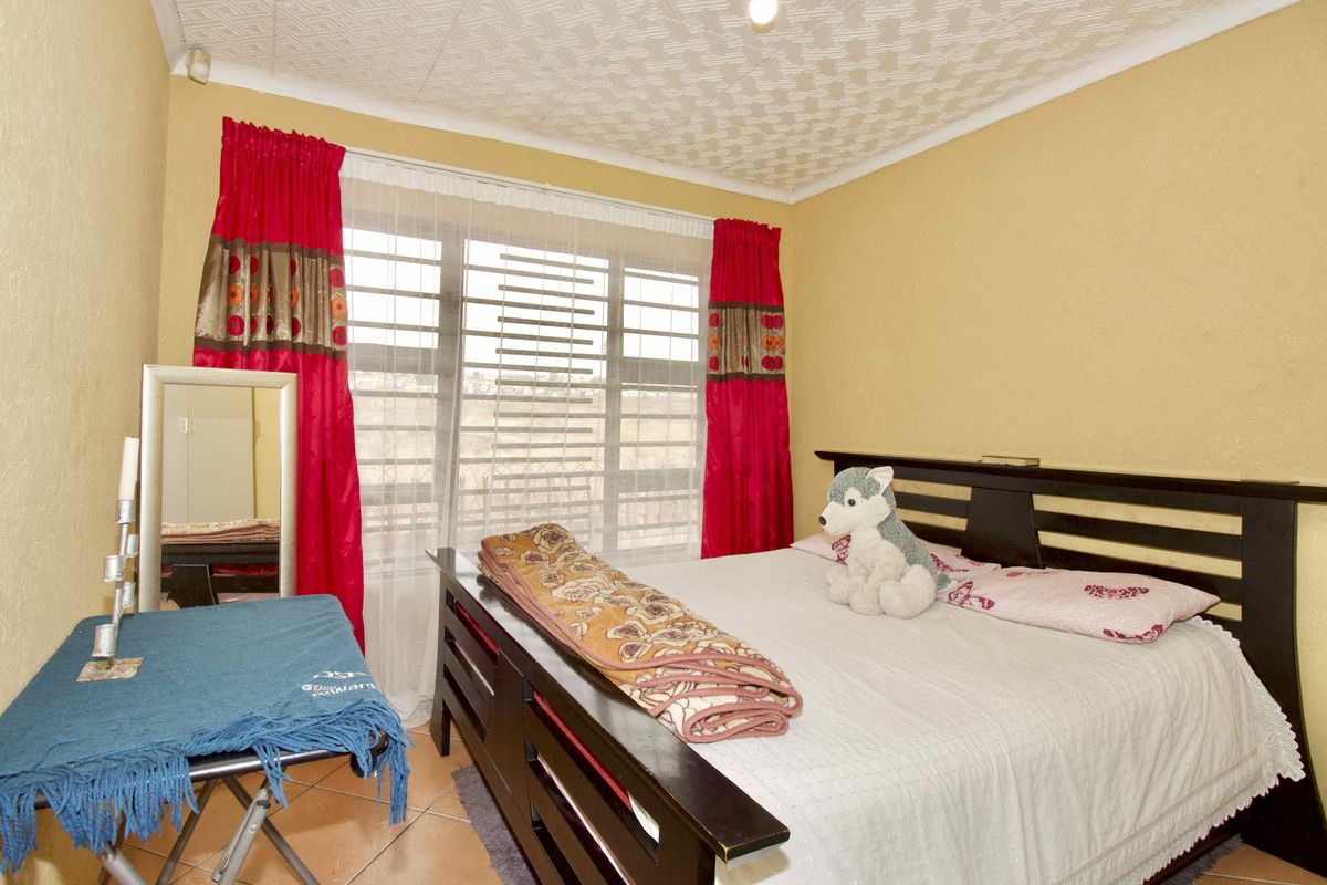 A bedroom featuring tiled flooring, a large window with natural light, and a textured ceiling finish.
