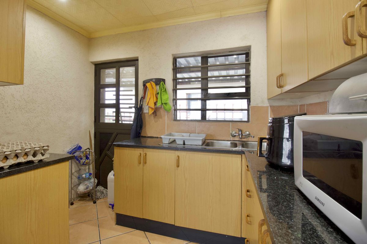 A functional kitchen featuring laminate cabinetry, granite countertops, a double sink, and security bars on the window.