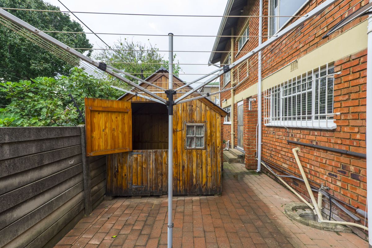 Rear exterior area featuring brick paving, a rotary clothesline, and a wooden garden shed adjacent to the main brick townhouse structure.