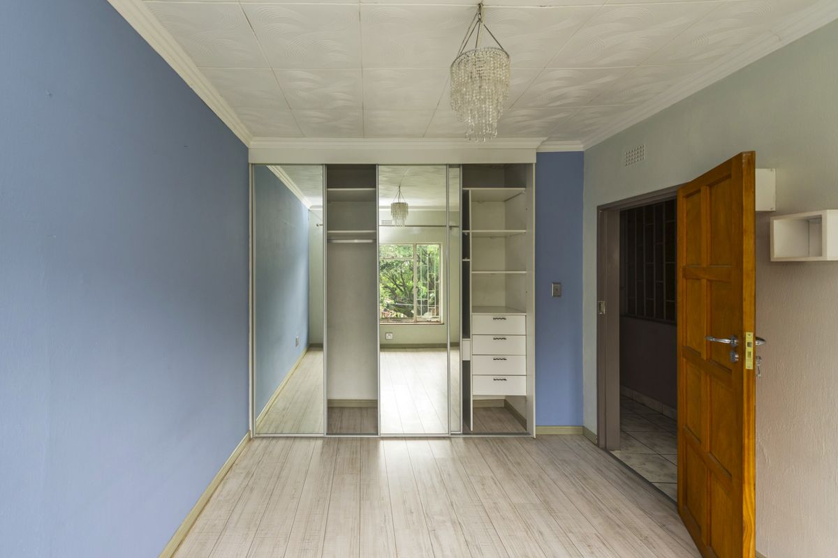 A vacant bedroom featuring built-in mirrored wardrobes, laminate flooring, and a classic ceiling rose, offering a clean canvas for personalization.