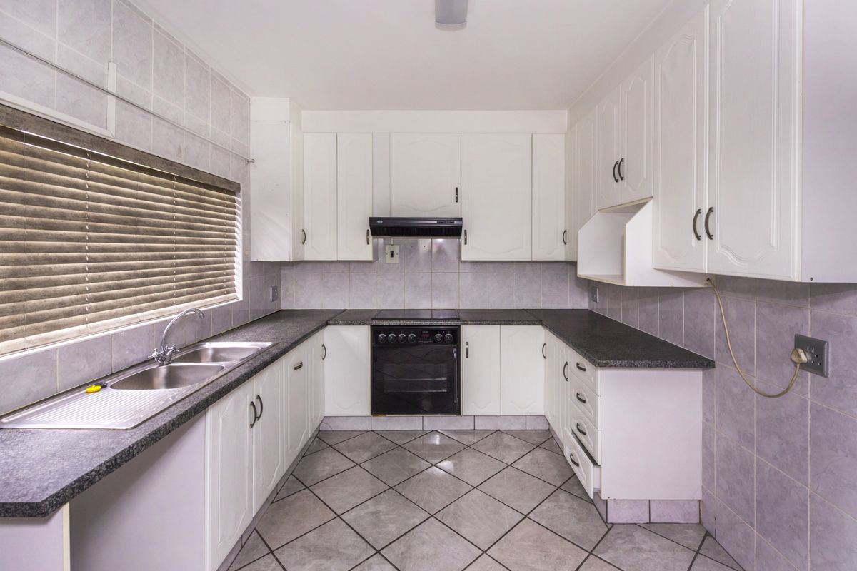 A functional kitchen featuring white cabinetry, dark laminate countertops, a built-in oven with extractor fan, and tiled flooring throughout.