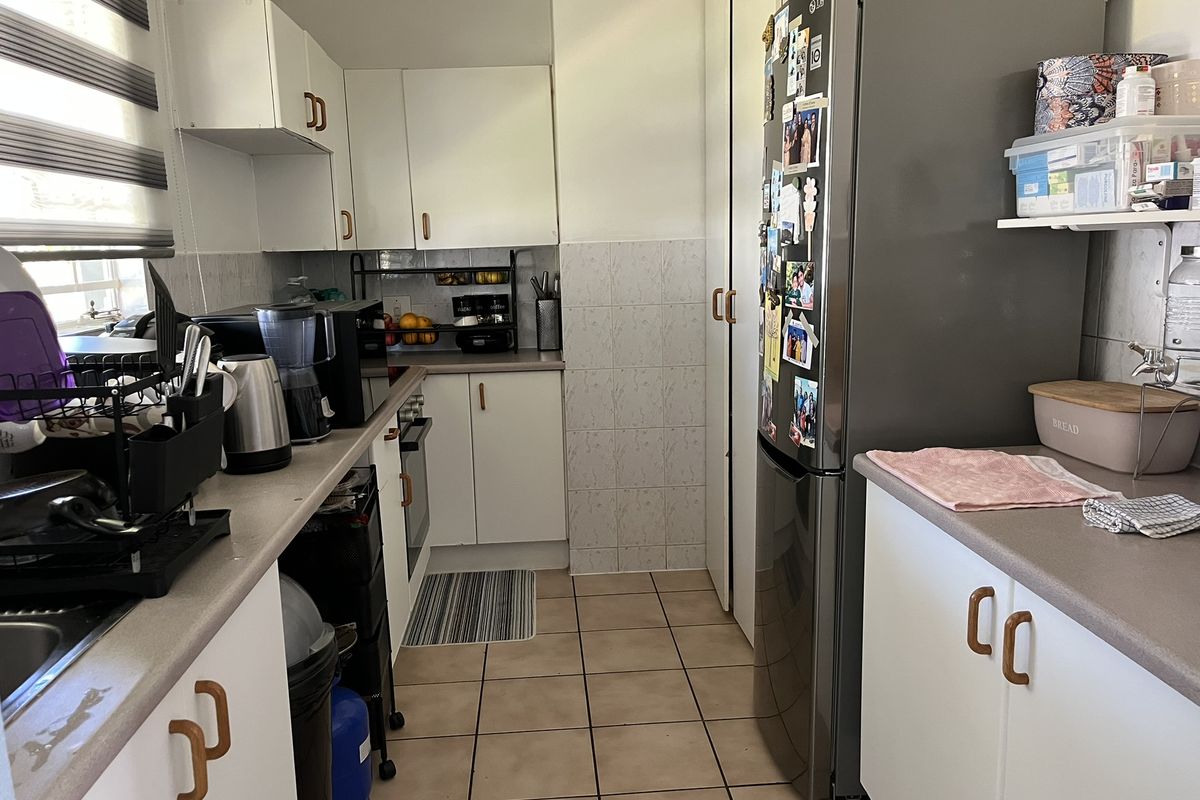 A functional galley-style kitchen featuring white cabinetry, tiled flooring, and a neutral countertop, providing efficient workspace and storage.