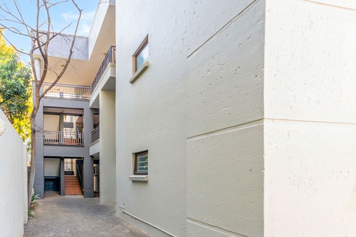 A view of the apartment complex exterior featuring a paved walkway, external staircases, and multi-level balconies with metal railings.
