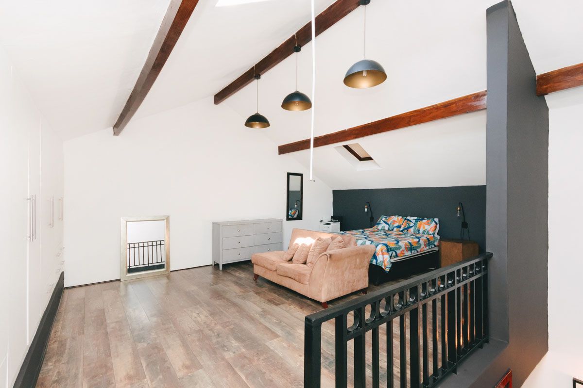 Spacious loft-style bedroom featuring exposed timber ceiling beams, a skylight, laminate flooring, and a secure metal balustrade overlooking the lower level.