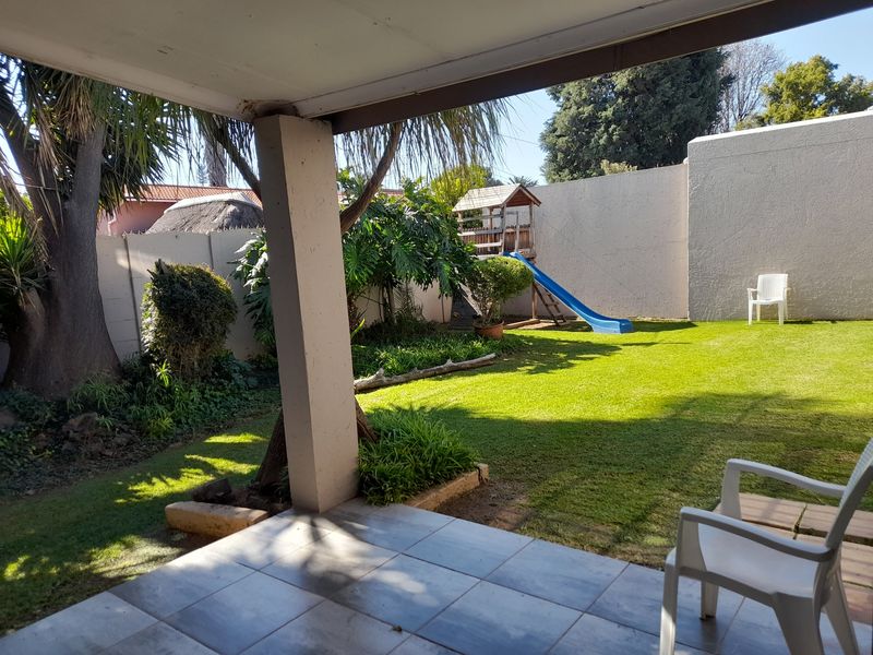A covered patio area overlooking a private garden with a lawn, mature trees, and perimeter boundary walls.