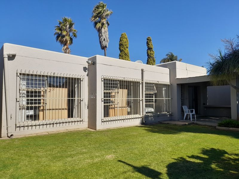 Rear view of the cluster property featuring a lawn, covered patio area, and security bars installed on the windows.