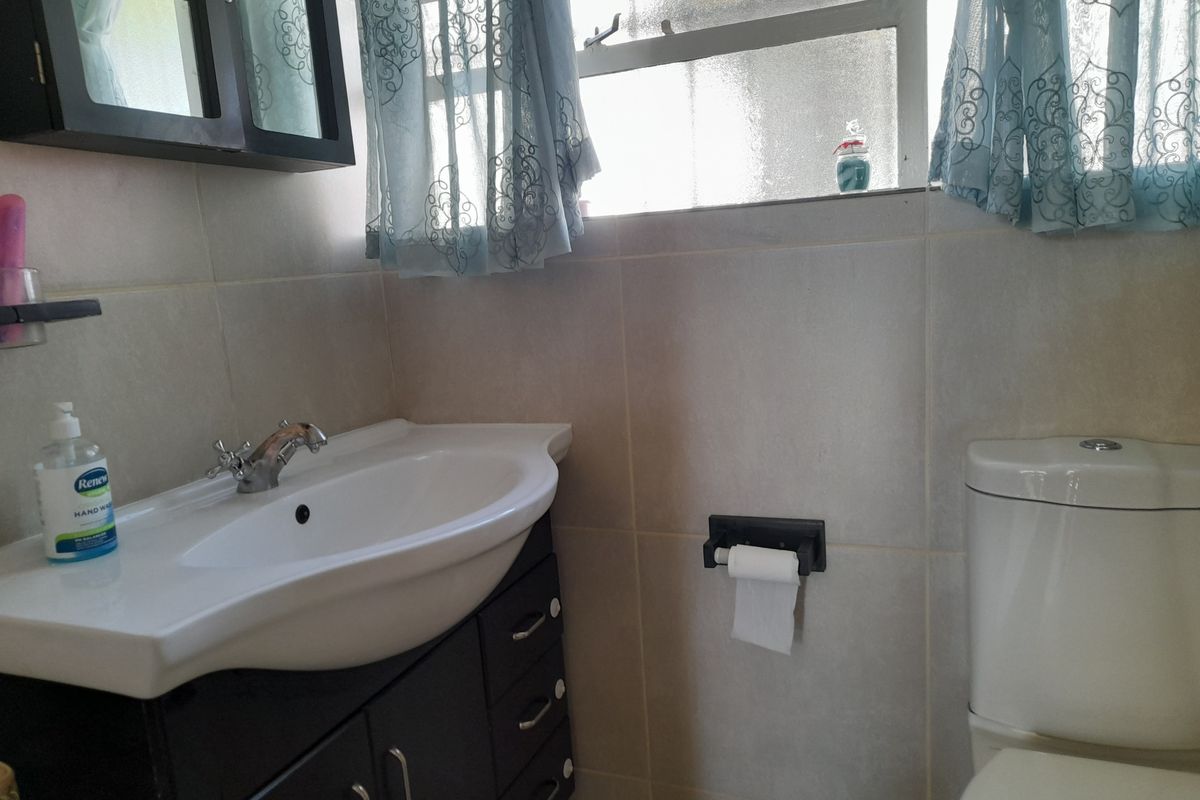 A functional bathroom featuring a vanity cabinet with a ceramic basin, chrome faucet, and a standard toilet, finished with neutral wall tiling.
