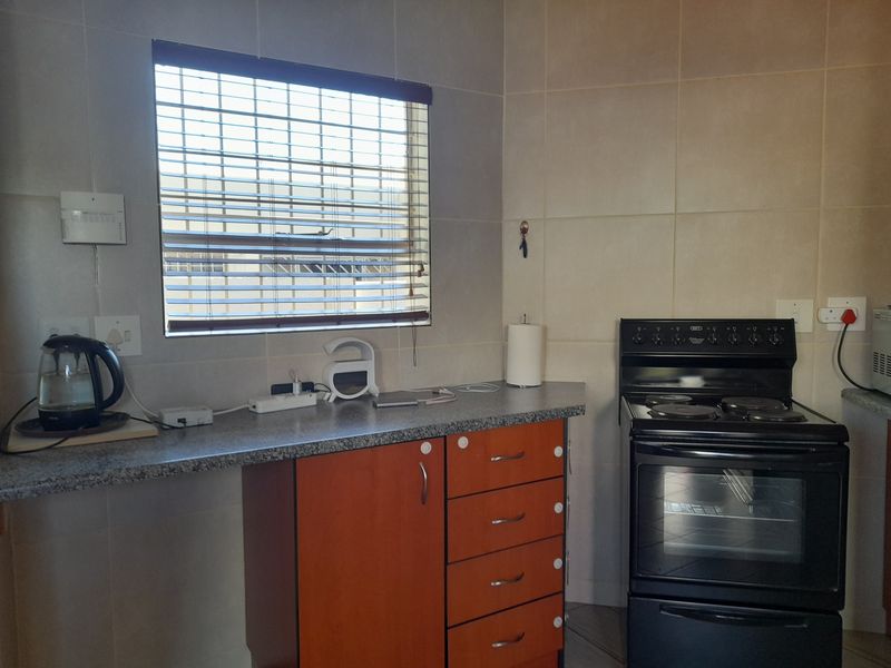 A functional kitchen area featuring tiled walls, laminate countertops, built-in cabinetry, and a freestanding electric stove.