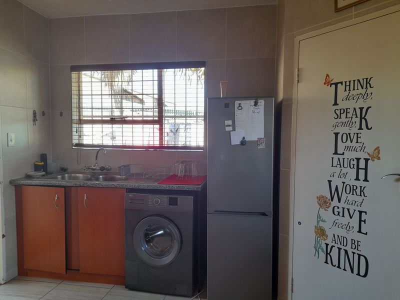 A functional laundry area featuring tiled walls and flooring, built-in cabinetry with a double sink, and space for a washing machine.