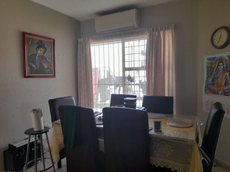 A dining area featuring a wall-mounted air conditioning unit and a window fitted with security bars.