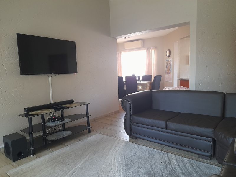 Open-plan living and dining area featuring tiled flooring and a wall-mounted air conditioning unit.
