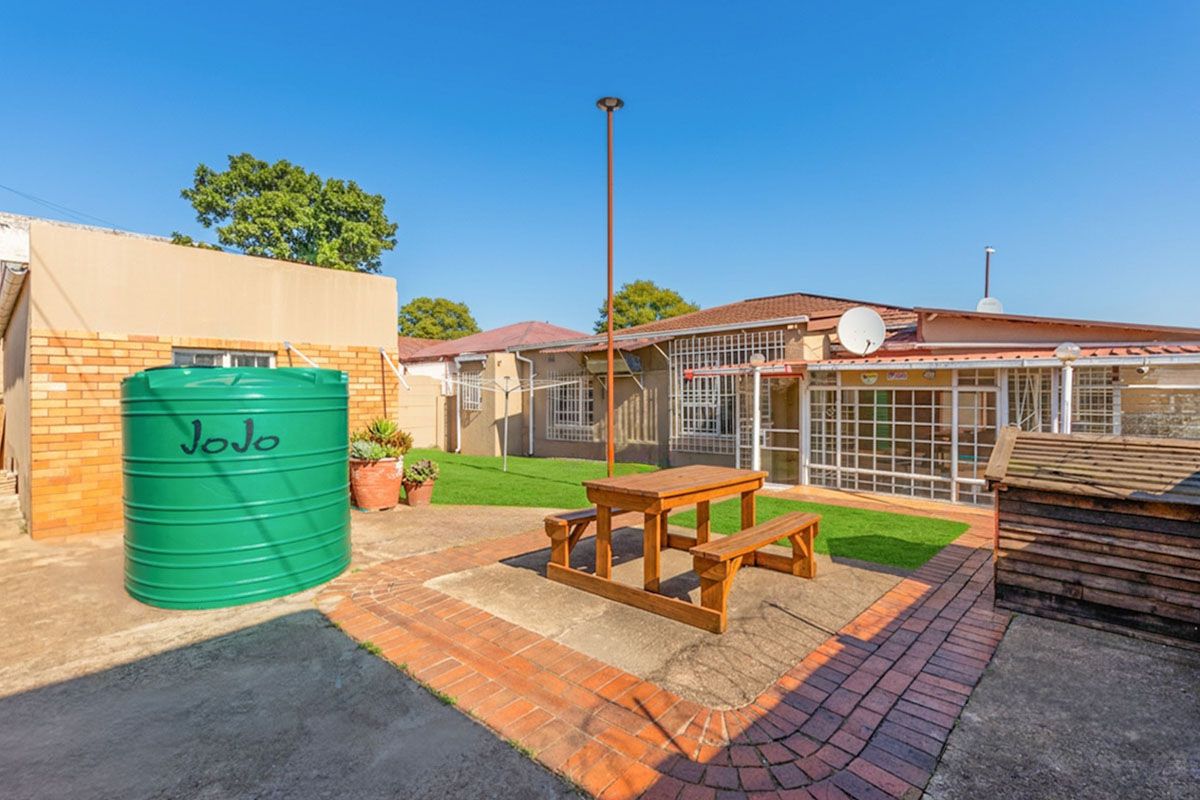 Rear exterior view featuring a paved patio area, green lawn, and a large water storage tank adjacent to the main dwelling.
