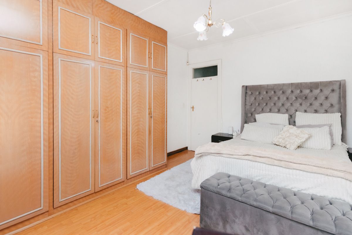 A well-maintained bedroom featuring extensive built-in wooden cabinetry, laminate flooring, and a classic transom door detail.
