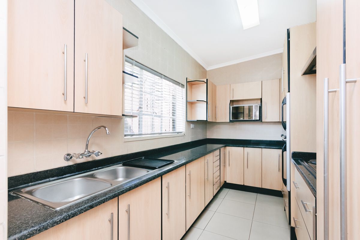 A functional kitchen featuring light wood-tone cabinetry, dark granite countertops, a double sink, and integrated appliances with neutral tiled finishes.