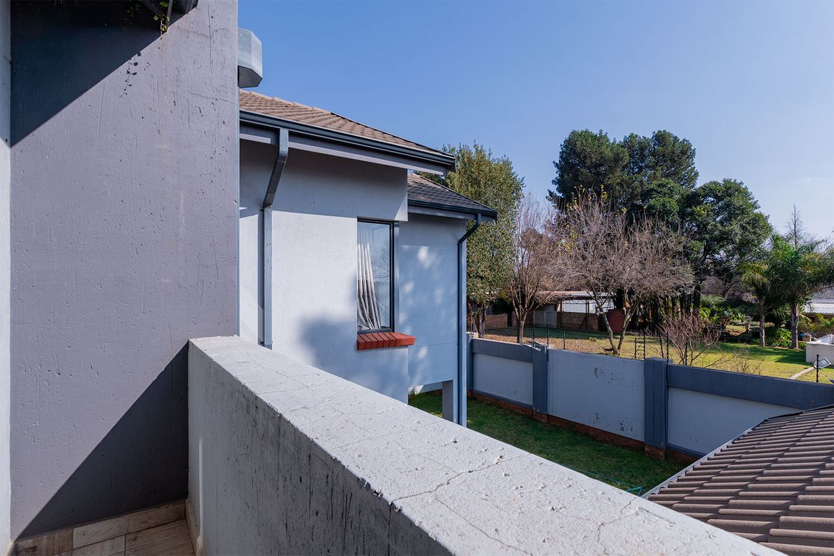 View from an upper-level balcony overlooking the rear garden, featuring a concrete boundary wall and tiled roof sections.