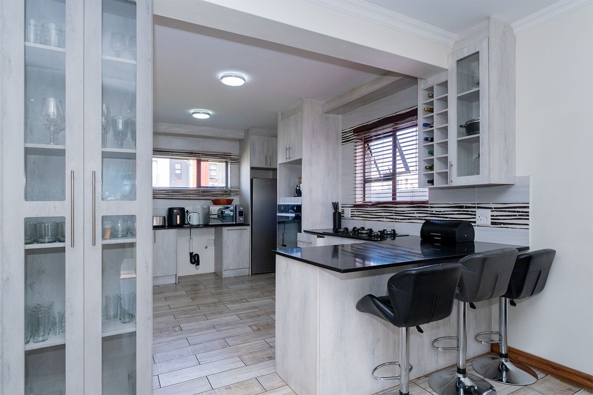 Modern kitchen featuring light wood-grain cabinetry, granite countertops, a gas hob, built-in oven, and integrated glass display shelving with a breakfast bar.