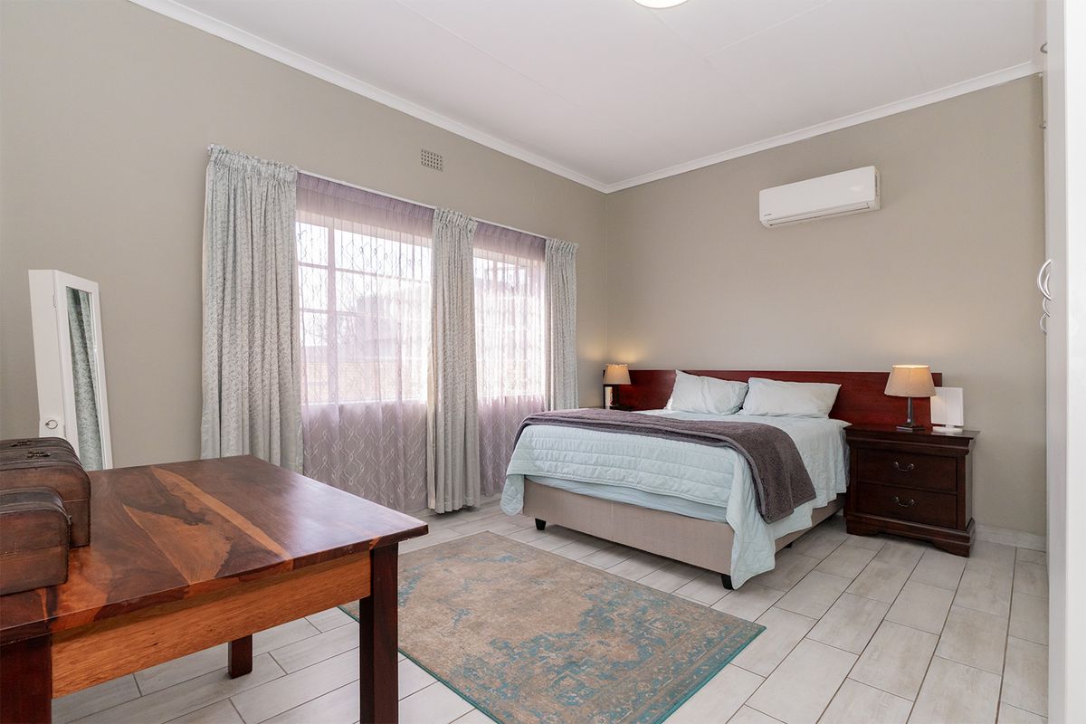 A well-maintained bedroom featuring tiled flooring, a wall-mounted air conditioning unit, and large windows with curtain tracks.