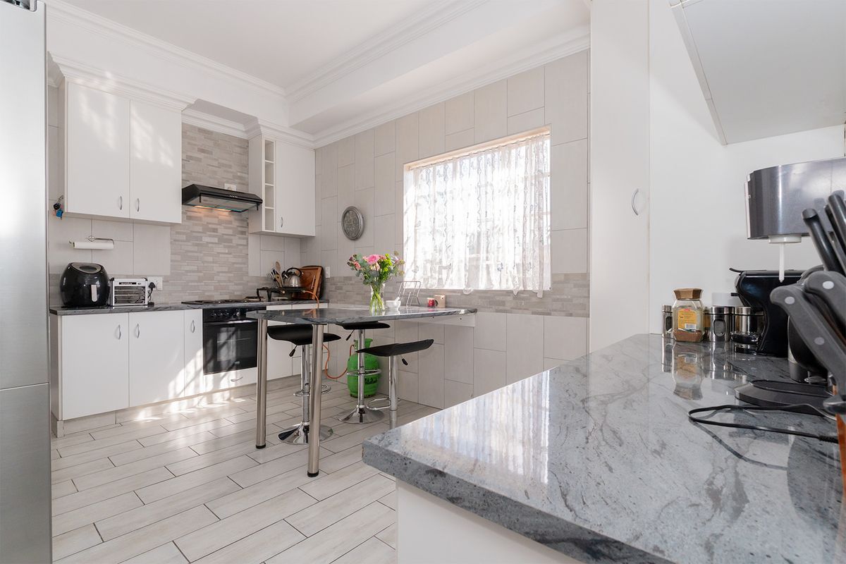 A bright, modern kitchen featuring white cabinetry, granite countertops, a built-in oven with extractor fan, and tiled flooring.