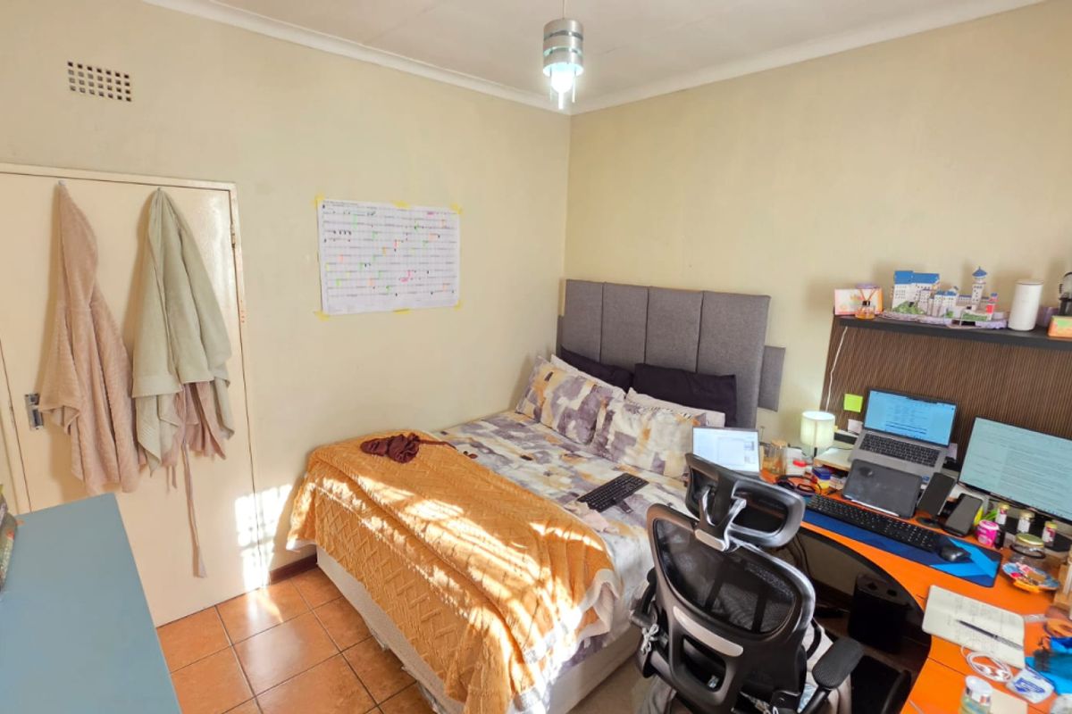 A functional bedroom featuring tiled flooring, a built-in headboard, and a dedicated workspace area.