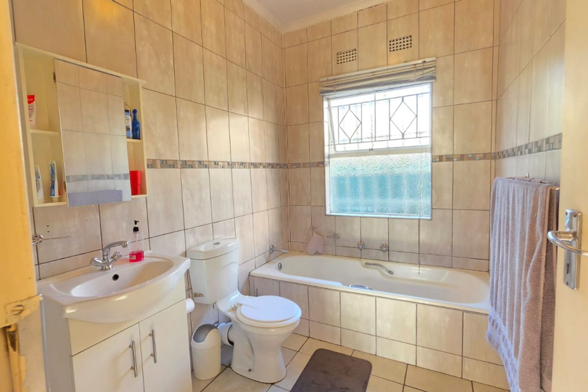 A functional bathroom featuring a built-in bathtub, pedestal vanity with integrated basin, and a toilet, finished with neutral wall and floor tiling.
