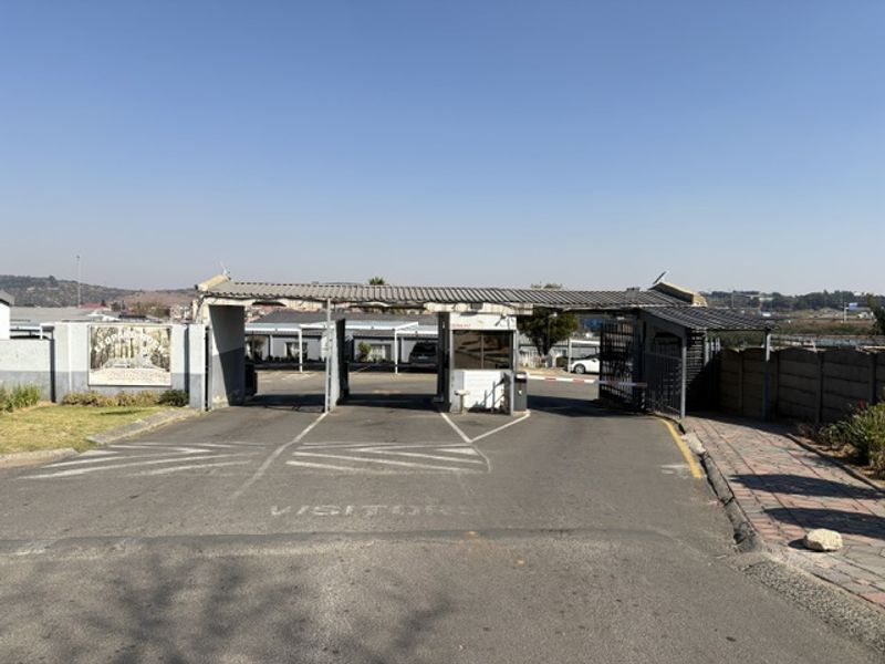 The main entrance to the apartment complex featuring a security guard house, boom gate access, and paved driveway.