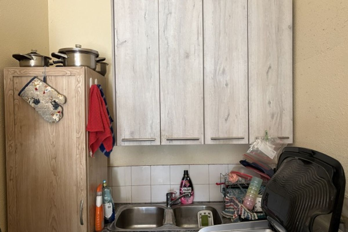 A functional kitchen area featuring a double bowl stainless steel sink, tiled splashback, and light wood-grain wall-mounted cabinetry.