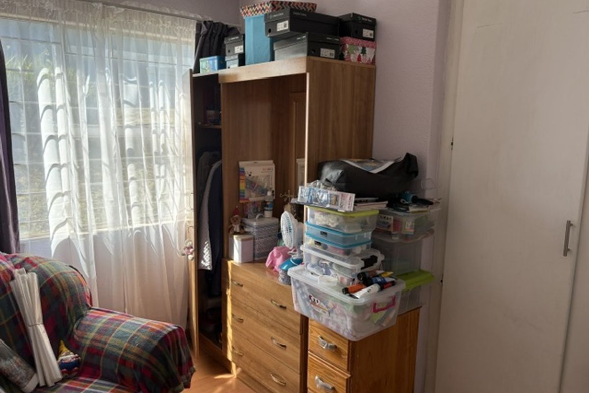 A bedroom featuring laminate flooring, a built-in wardrobe, and a window fitted with security bars.