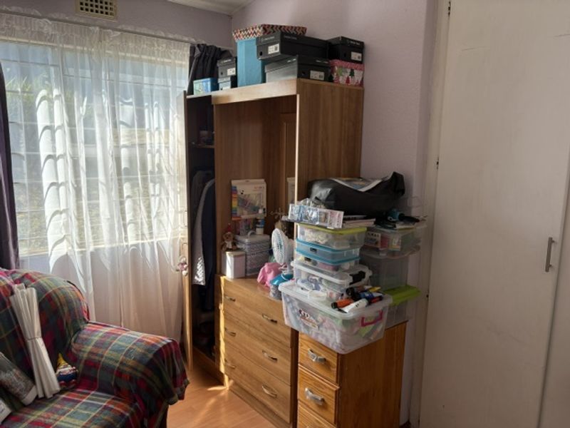 A bedroom featuring laminate flooring, a built-in wardrobe, and a window fitted with security bars.