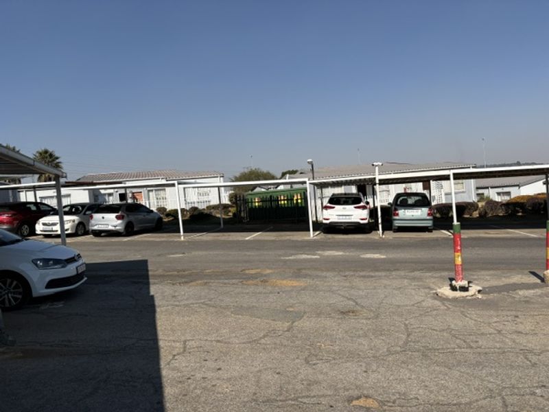 Exterior view of the apartment complex parking area featuring covered carports and an asphalt driveway.