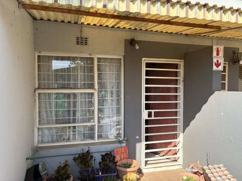 Front entrance area featuring a security gate, security bars on the window, and a corrugated roof covering.