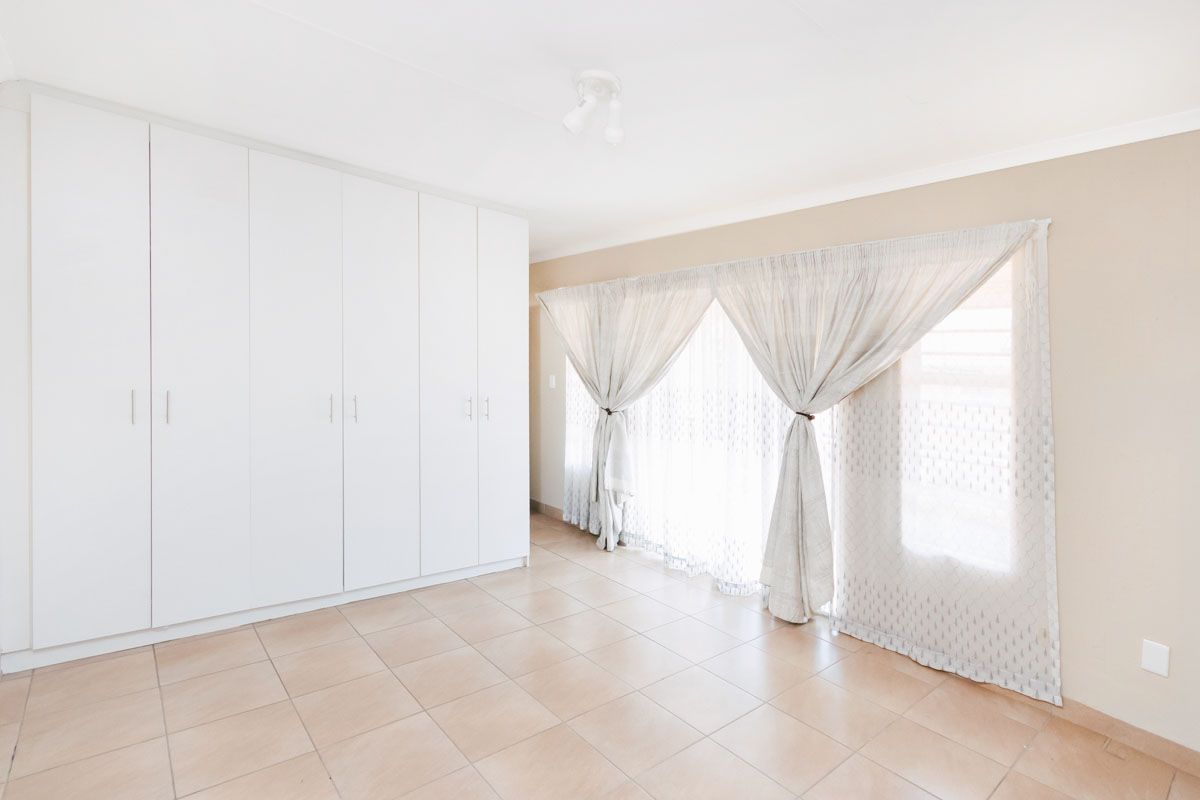 A bright, empty bedroom featuring neutral tiled flooring and extensive white built-in cupboards, offering a clean and versatile space.