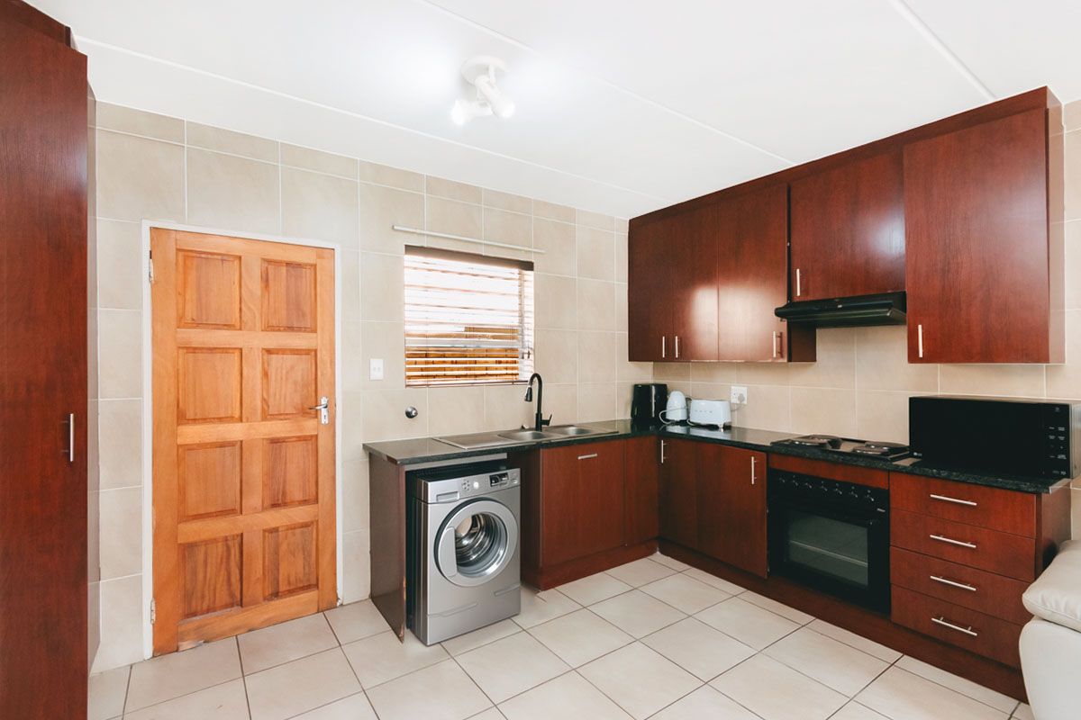 A functional kitchen featuring dark wood cabinetry, granite countertops, tiled backsplash, and integrated appliances, including an oven, hob, and extractor fan.