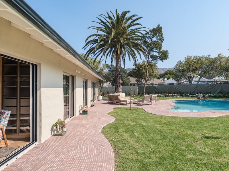 A spacious rear garden featuring a swimming pool, curved brick patio, and established palm tree, accessible via large sliding glass doors.