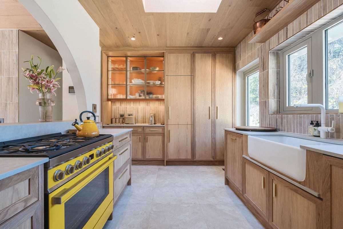 A beautifully crafted kitchen featuring custom oak cabinetry, a farmhouse sink, stone countertops, and a striking yellow range cooker under a timber-clad ceiling.
