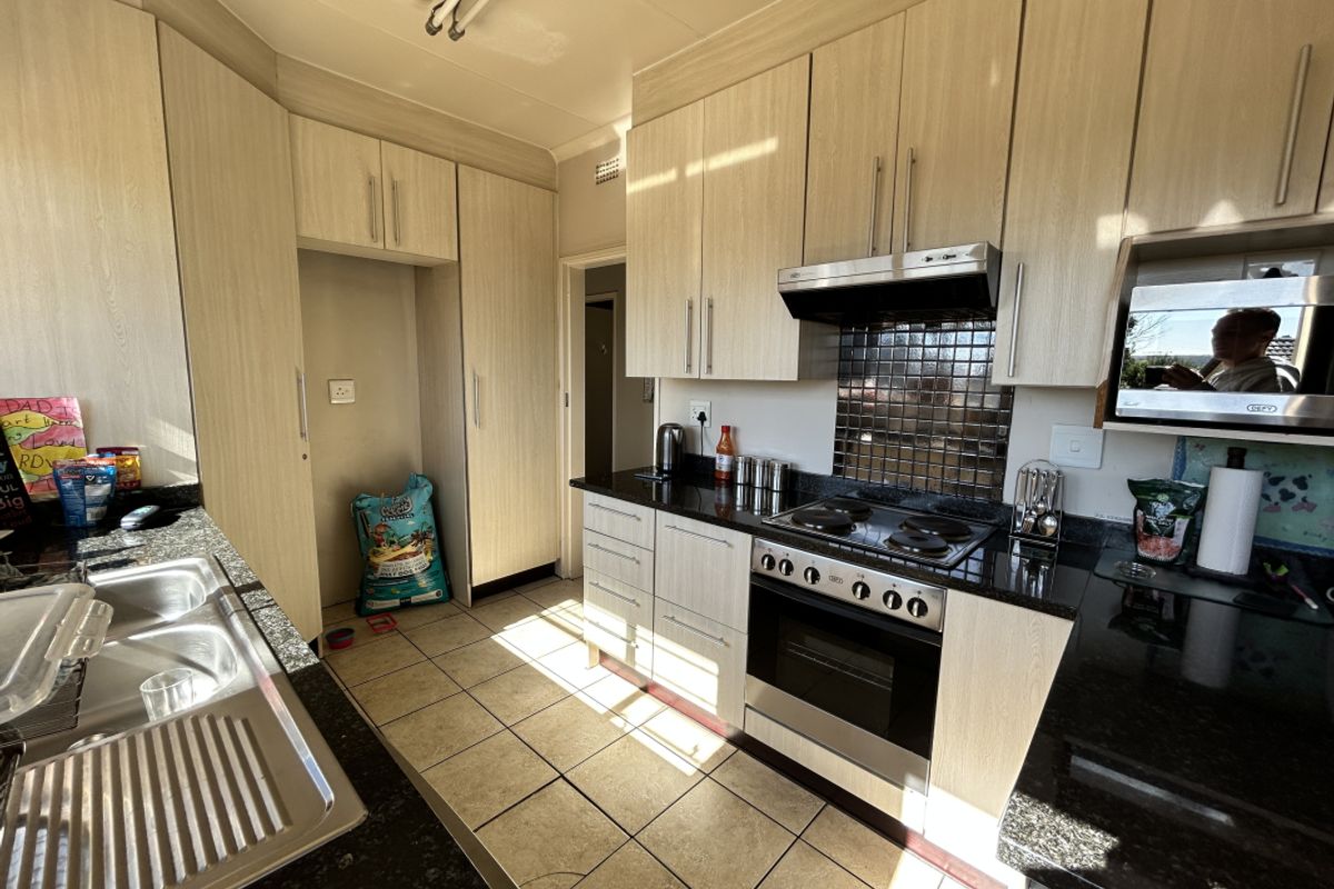 Functional kitchen featuring light wood-grain cabinetry, dark granite countertops, a built-in oven with extractor fan, and tiled flooring.