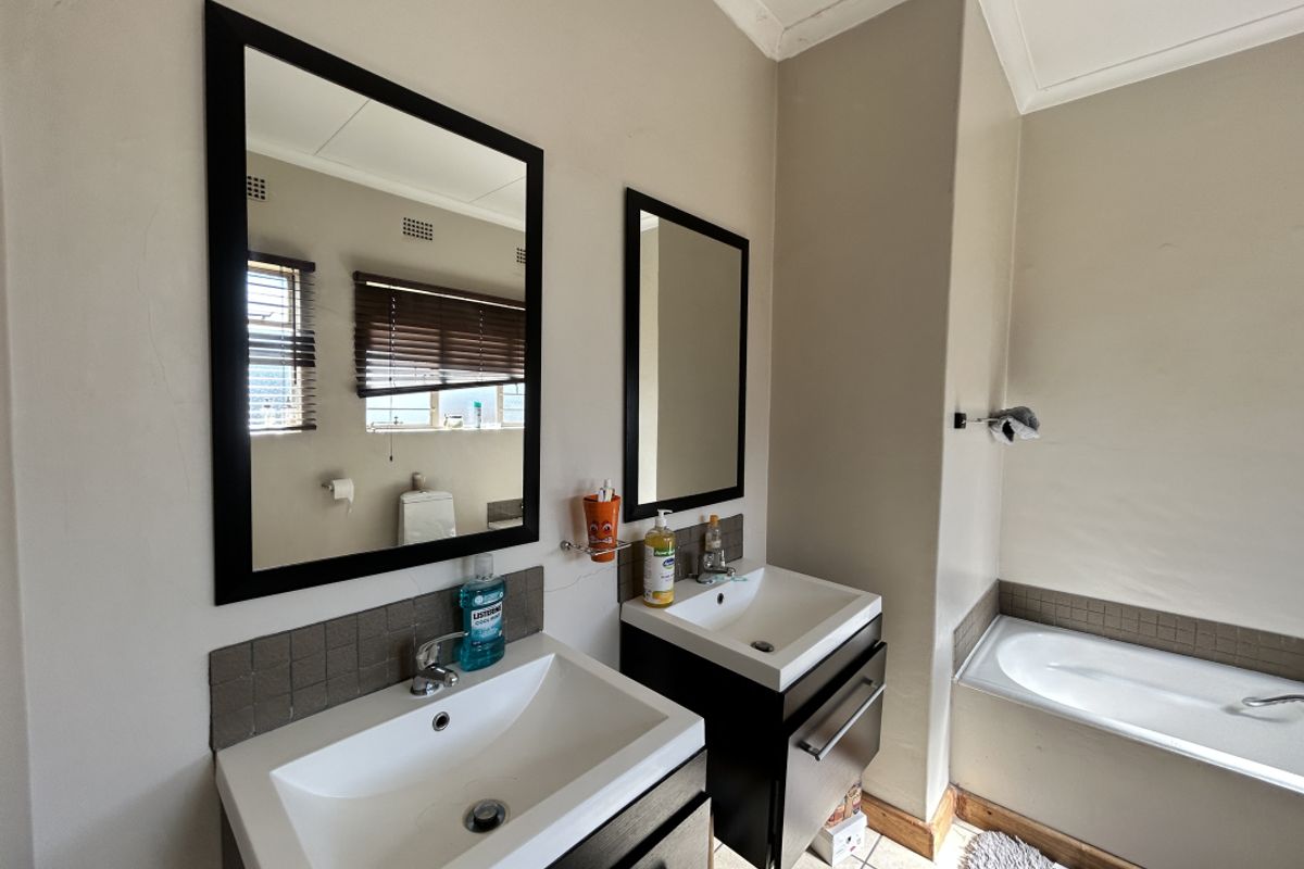 Bathroom featuring a double vanity with modern basins, dark cabinetry, framed mirrors, and a tiled bathtub surround.