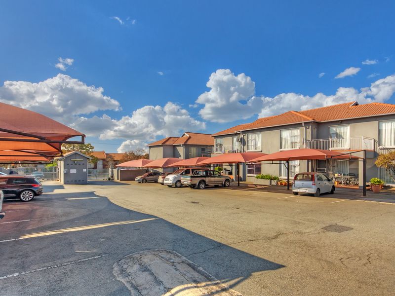 Exterior view of the apartment complex featuring a paved parking area with covered carports and multi-story residential units.