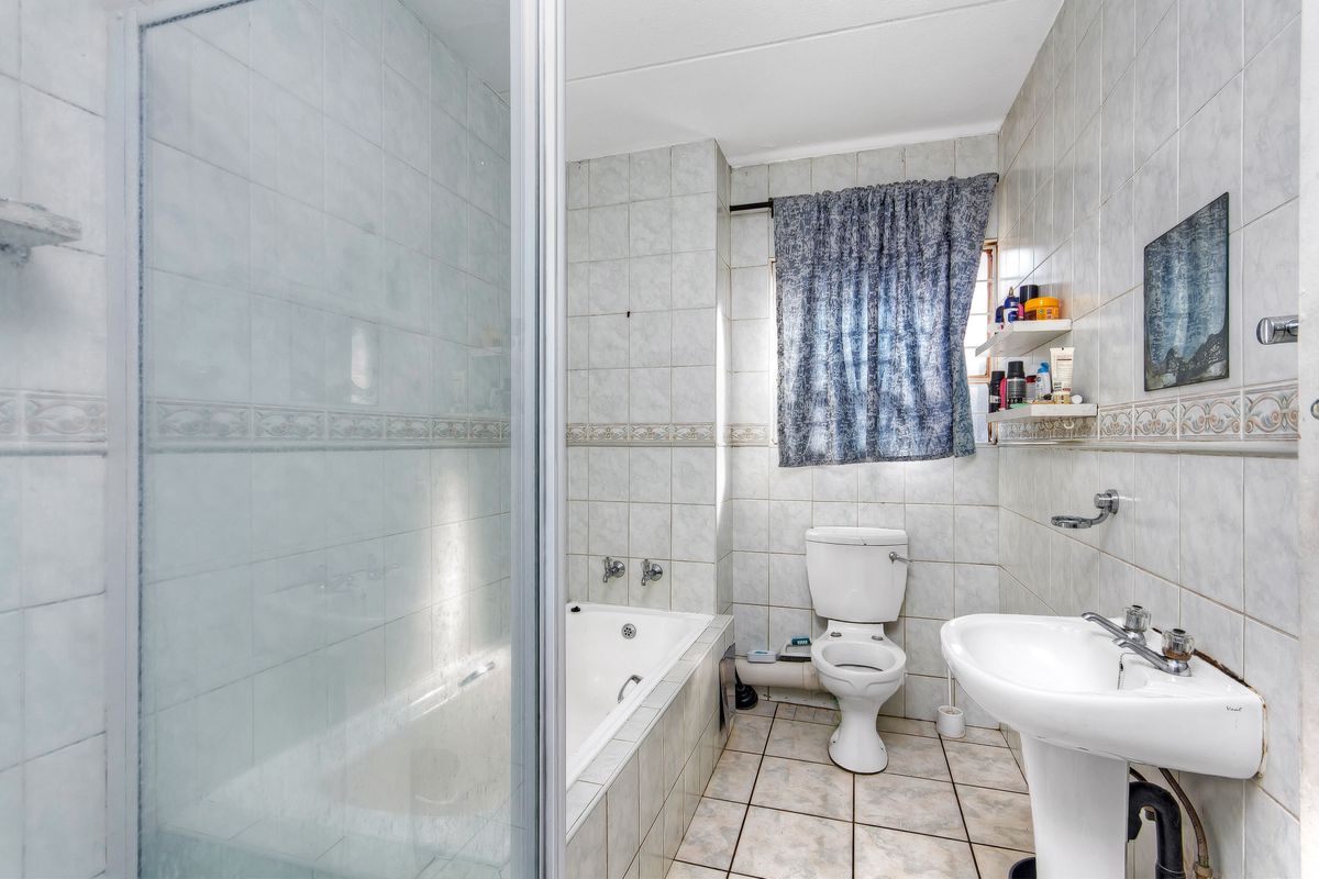 A functional bathroom featuring a pedestal basin, a built-in bathtub with a glass shower enclosure, and tiled finishes throughout.
