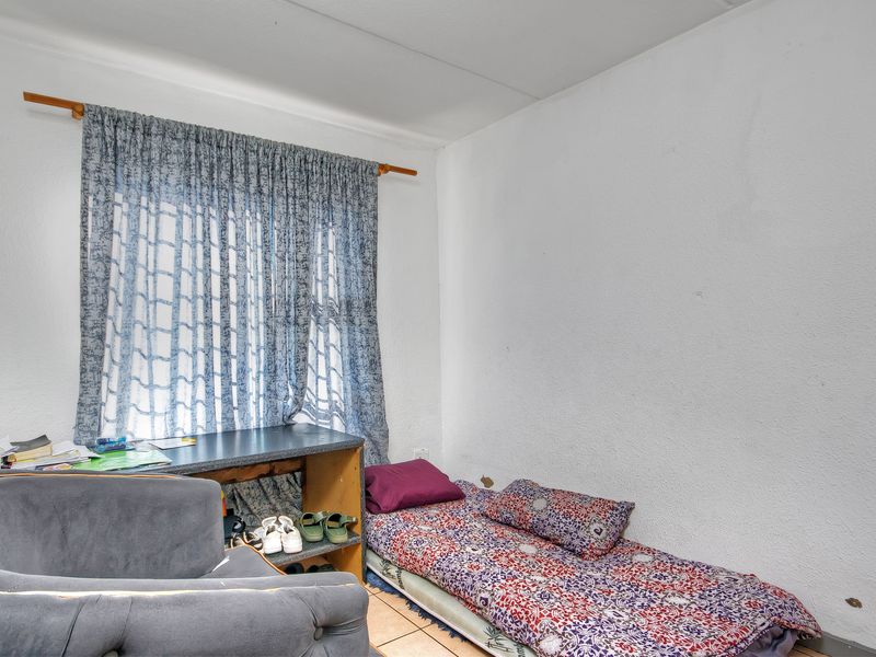 A compact bedroom featuring tiled flooring and a window with a curtain rod, requiring minor wall repairs and cosmetic updates.