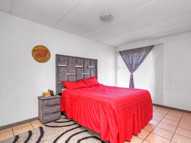 A bedroom featuring tiled flooring and a standard ceiling light fixture, requiring cosmetic updates to improve the overall finish and appeal.