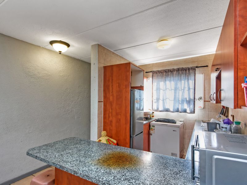 A functional kitchen featuring laminate cabinetry, granite countertops, and tiled backsplash, offering a practical layout with potential for cosmetic updates.