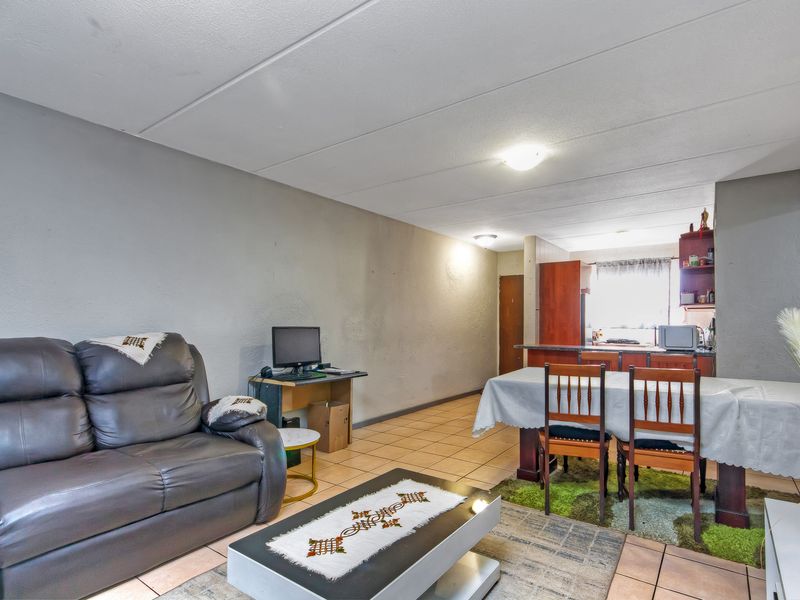 Open-plan living and dining area featuring tiled flooring and an adjoining kitchen with built-in cabinetry and a breakfast counter.