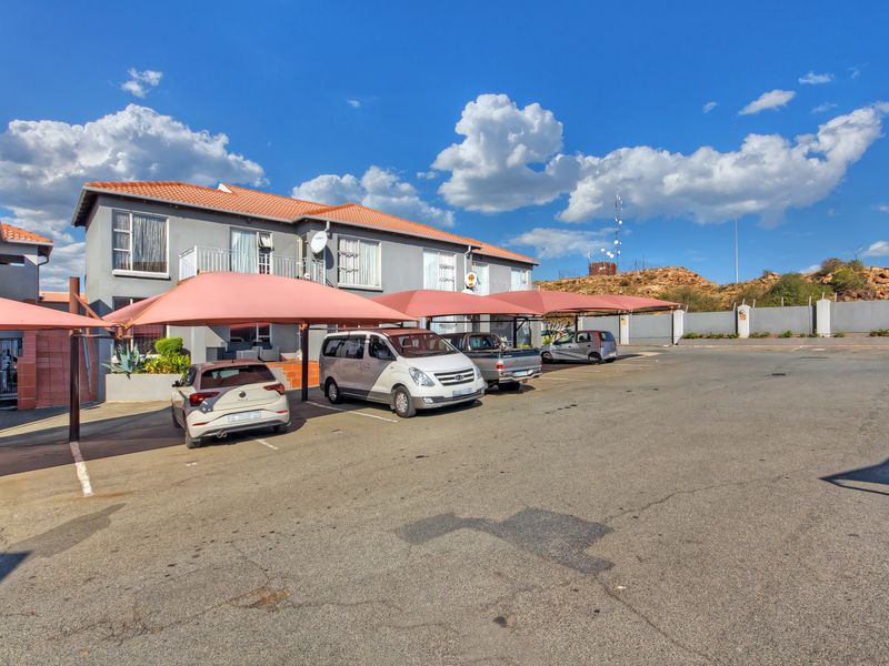 Exterior view of the apartment complex featuring a paved parking area with shade cloth carports and a perimeter boundary wall.