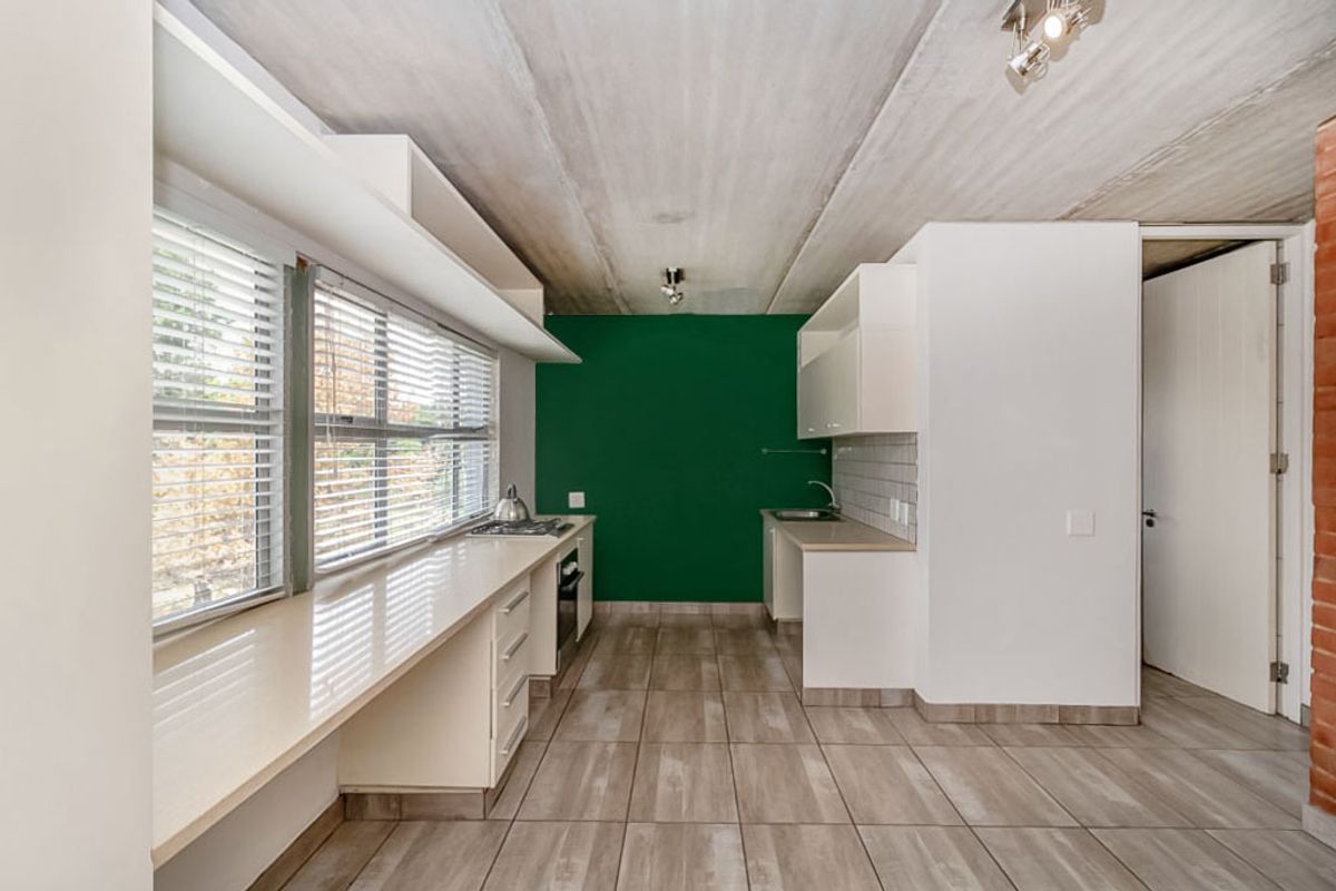 Modern kitchen featuring built-in cabinetry, stone countertops, integrated hob and oven, tiled flooring, and an exposed concrete ceiling with a bold green accent wall.