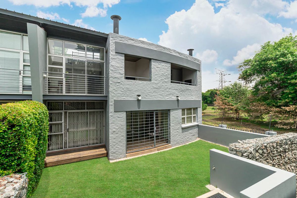 Rear view of a modern apartment building featuring a textured grey facade, timber decking, a private lawn, and secure balcony access.