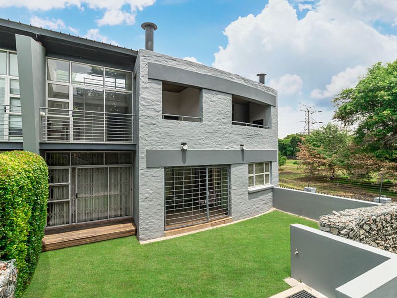 Rear view of a modern apartment building featuring a textured grey facade, timber decking, a private lawn, and secure balcony access.